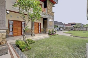 Una casa de dos pisos con entrada pavimentada, un pequeño césped y un árbol en el jardín delantero.