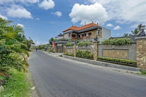 Una calle residencial con una casa de dos pisos, un muro de piedra y cielo despejado.