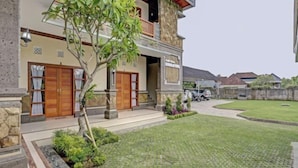 Ein zweigeschossiges Haus mit einer Stein-Fassade, Holztüren und einem kleinen Garten mit gepflastertem Bereich und einem Baum.