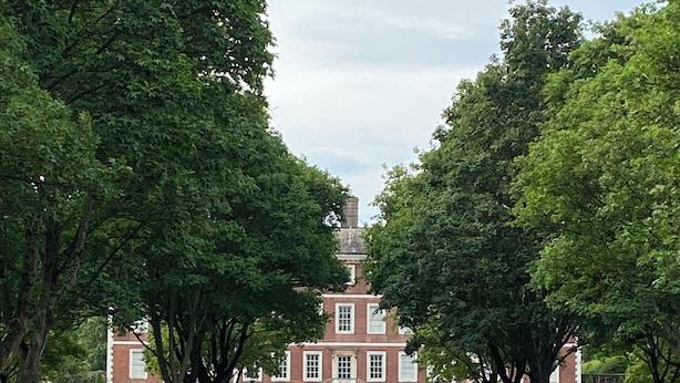 A symmetrical building with a central staircase, flanked by trees and manicured hedges.