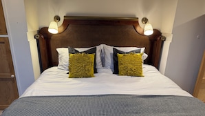 A neatly made bed with a striped bedspread, two large floral pillows, and two wall-mounted lamps.