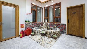 Un vestíbulo con una zona decorativa central, una puerta de madera y un extintor.