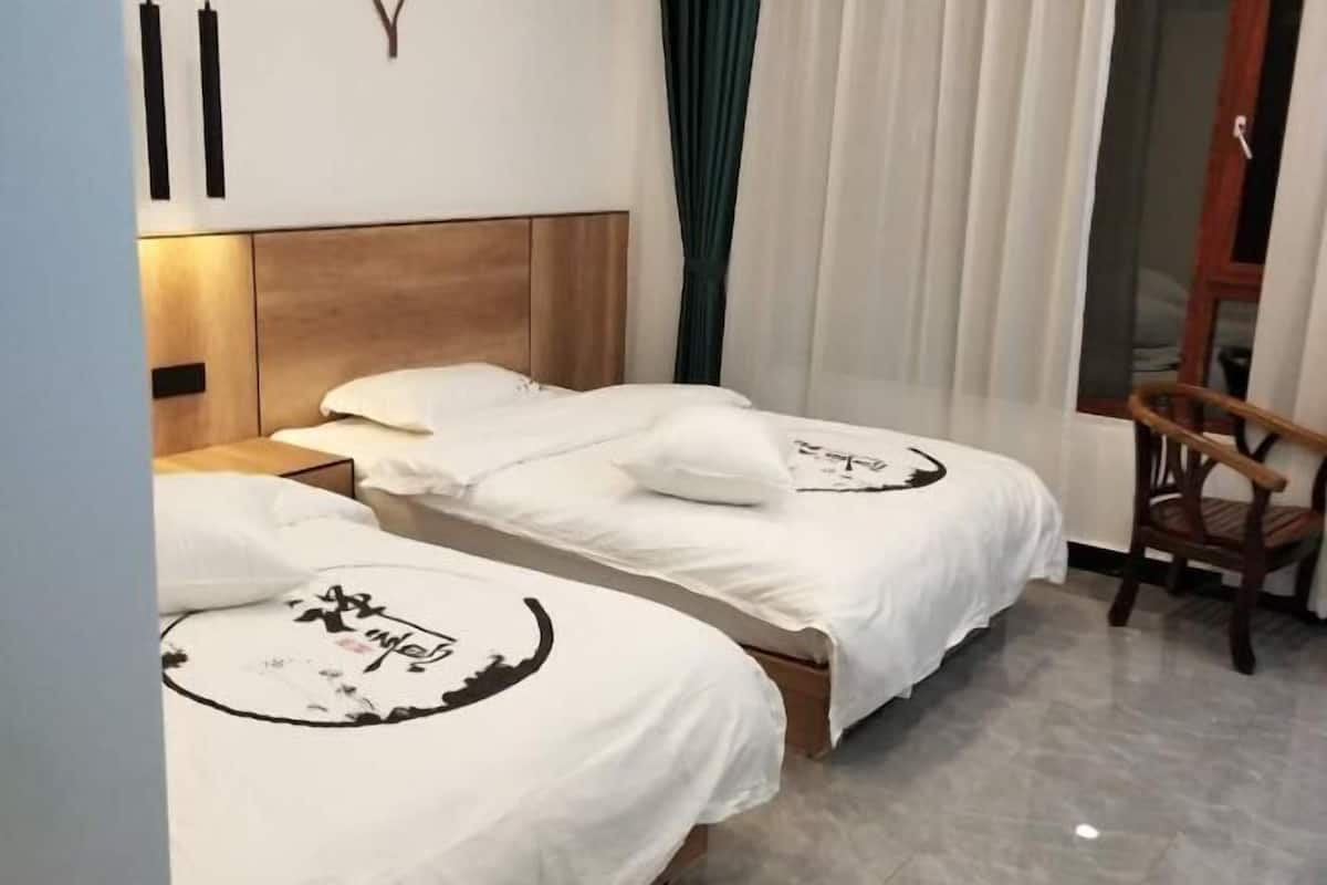 Hotellihuone, jossa on kaksi erillistä sänkyä, puinen pääty ja puinen tuoli sekä ikkuna, jossa on verhot.