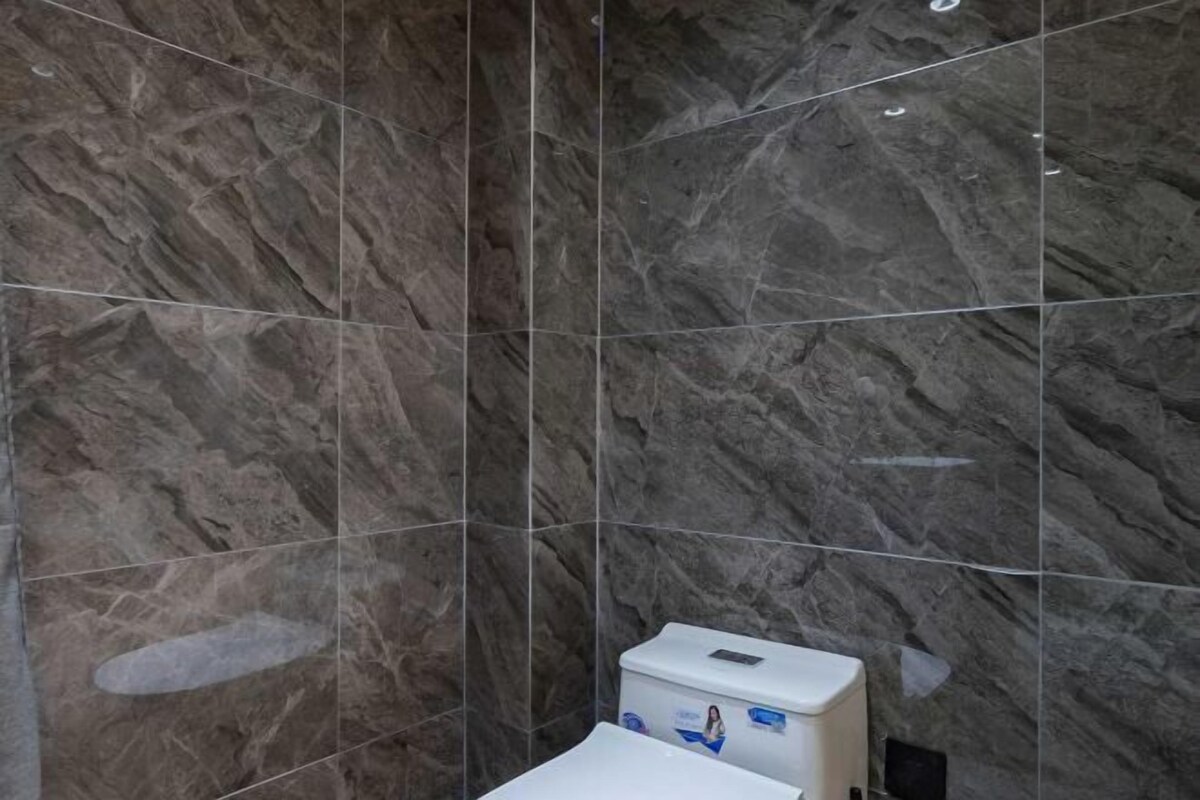 Casa de banho com azulejos de mármore escuro e uma pia branca com dispensador de sabonete.