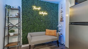 A modern living room with a green wall, a sofa, a side table, and a decorative shelf. - Private Garden Retreat - King Bed - mins TMH + Downtown + FSU! (Tallahassee)