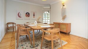 Zona pranzo con tavolo e sedie in legno, tappeto decorato e mobiletto in legno.