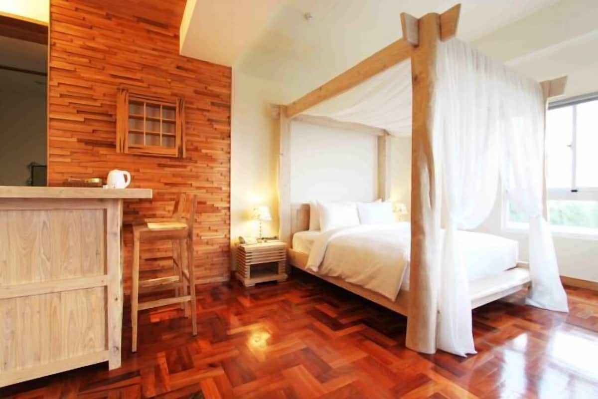 A room with a wooden herringbone floor, a bed with white bedding, a nightstand with a lamp, and a wooden cabinet.