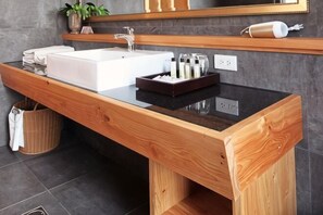 Un baño moderno con tocador de madera, un lavamanos blanco y un espejo encima.