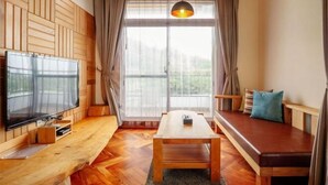 Ein gemütliches Zimmer mit Holzboden, einem Fernseher links, einer Bank mit Kissen und einem Tisch.