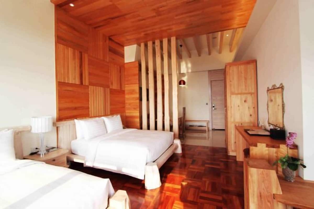 A modern hotel room with a wooden ceiling, a large bed, a wooden desk, and a mirror.