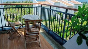 Ein Balkon mit Holzstuhl und Tisch, Blick auf das Meer und weiße Gebäude im Hintergrund.