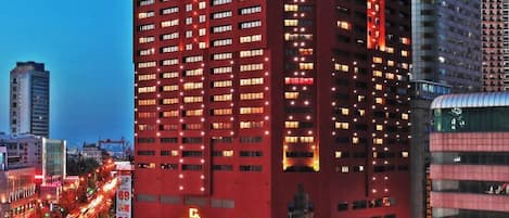 A high-rise building with multiple floors and numerous windows, surrounded by a busy urban environment with visible traffic and other buildings.