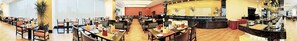 Un vaste espace de restauration de l’hôtel, doté de nombreuses tables et chaises, d’un bar central et offrant une vue sur le hall d’entrée.