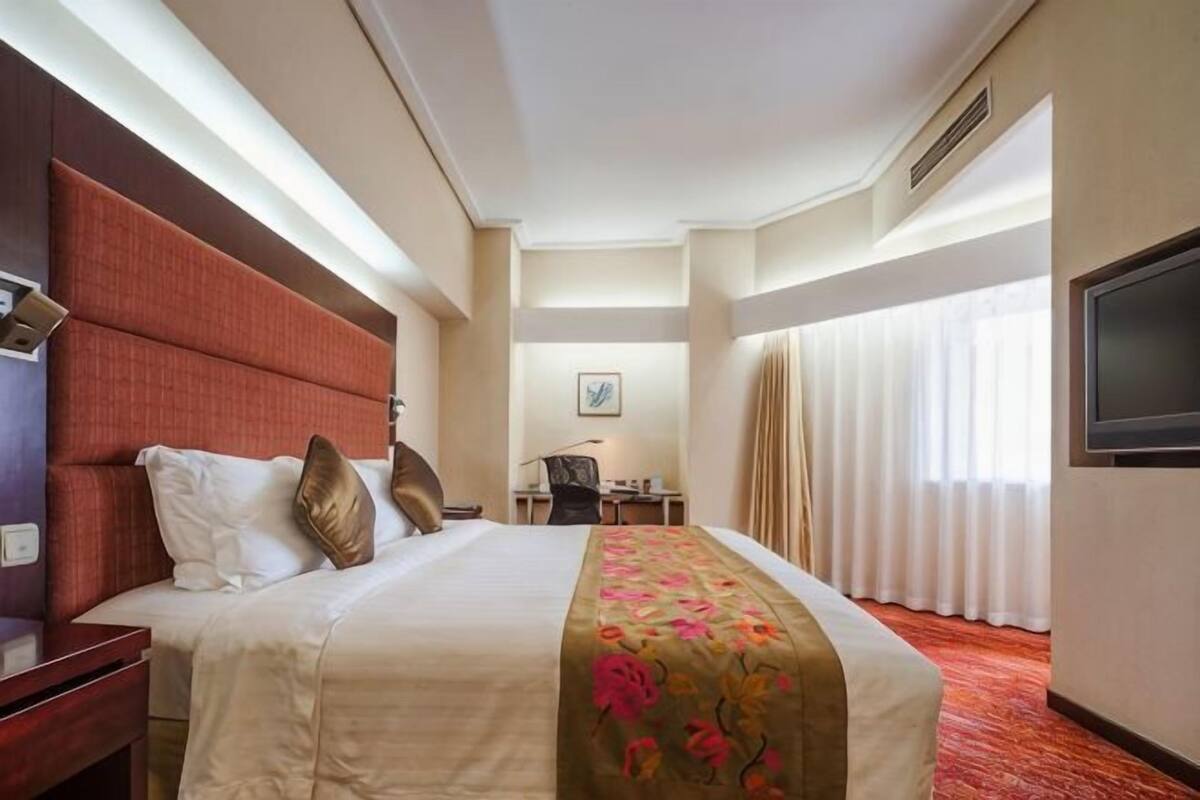 Een hotelkamer met een groot bed, een bureau, een stoel, een televisie en een raam met gordijnen.