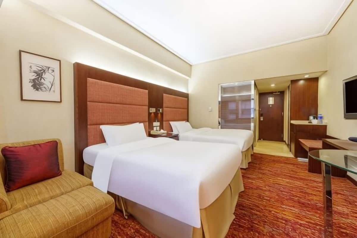 A hotel room with two beds, a sofa, a desk, and a TV.