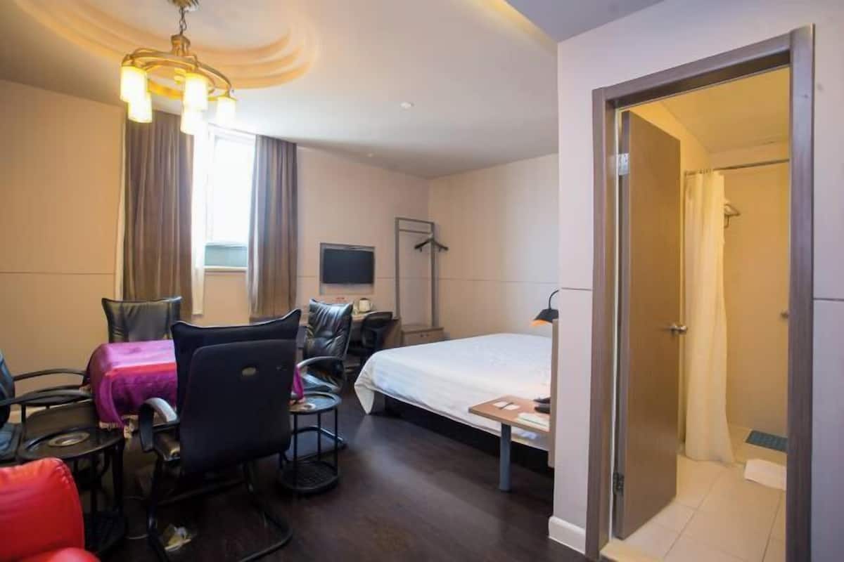 A hotel room with a bed, a desk with a chair, a TV, and a wardrobe.