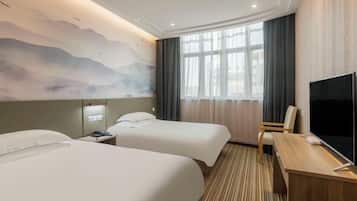 A hotel room with two beds, a desk, a TV, and a large window with curtains.