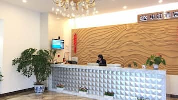A hotel reception area with a modern design, including a reception desk, a large potted plant, and a wall-mounted television.