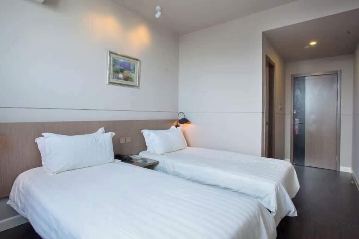 A hotel room with two beds, a nightstand, a wall-mounted lamp, and a door leading to another room.