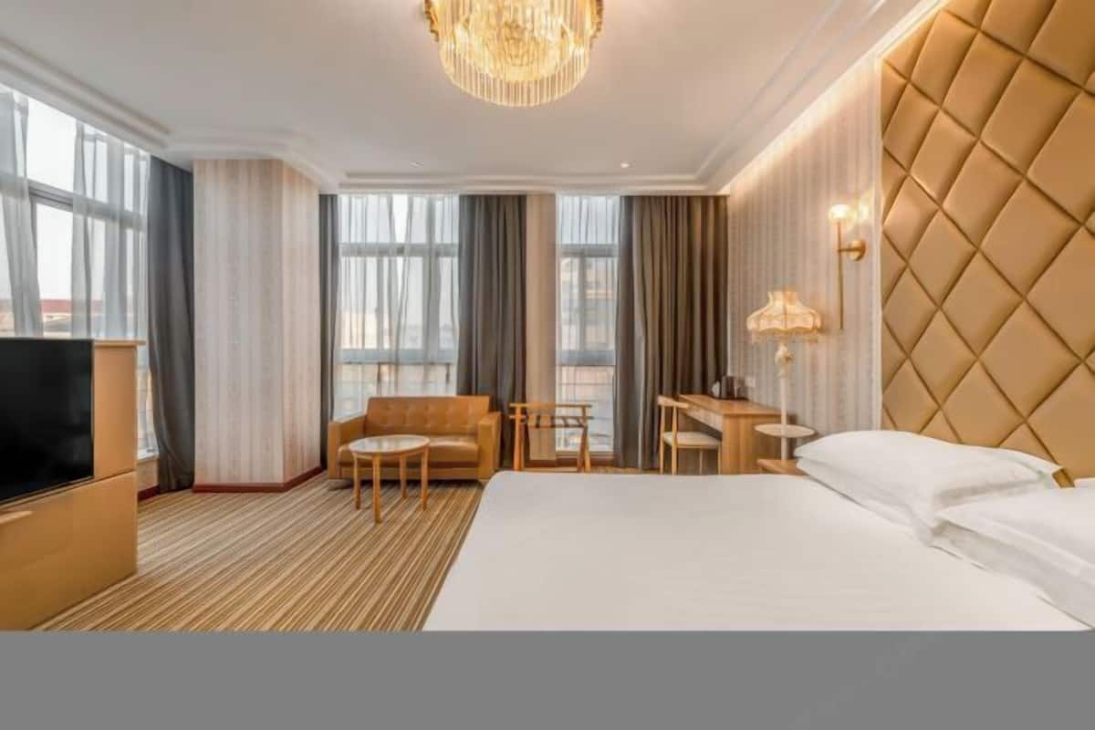 A hotel room with a large bed, a desk, a sofa, a TV, and a chandelier.
