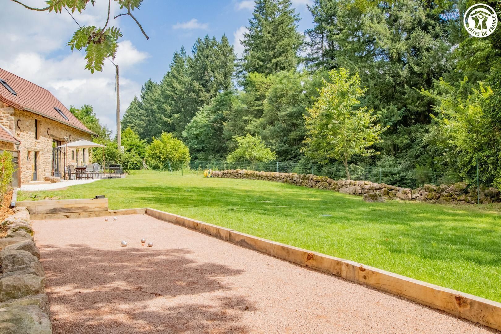 Une cour avec un terrain de pétanque, des murs en pierre et un bâtiment en pierre doté d’un espace extérieur aménagé pour s’asseoir.