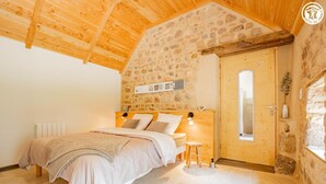Un dormitorio con pared de piedra, techo de madera y una cama con mesita de noche.