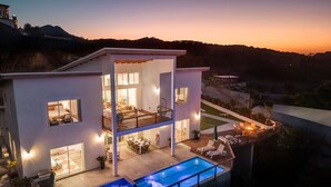 Una casa moderna de dos pisos amb piscina, zona d'estar a l'aire lliure i vistes a les collines.