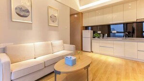 A modern living room with a sofa, a small table, and a kitchen area with cabinets and appliances. - Wuhan Boya Ward Hotel (Optics Valley Convention and Exhibition Center Joy City Branch) (Wuhan)