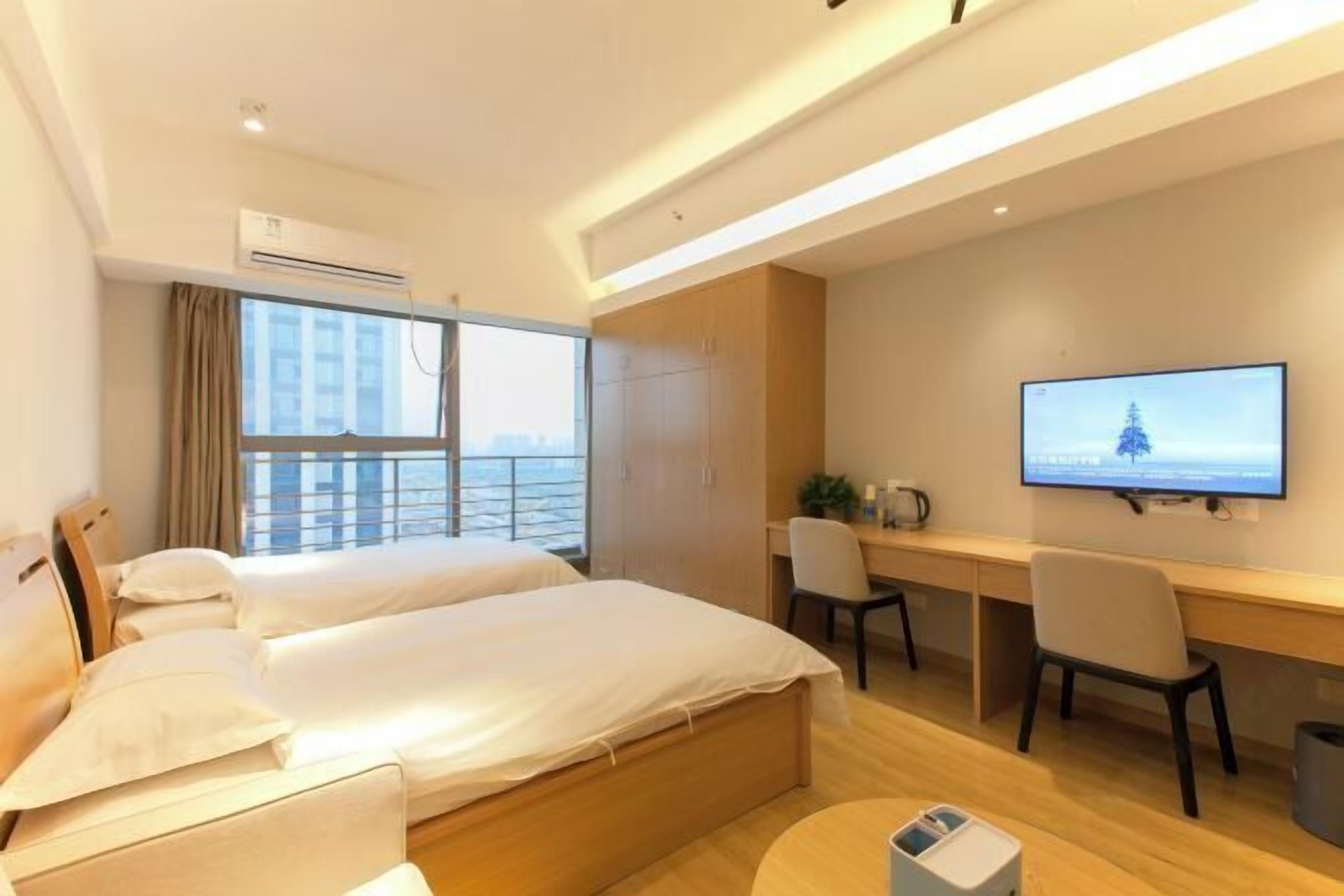 A hotel room with two beds, a desk, a chair, a TV, and a window with curtains.