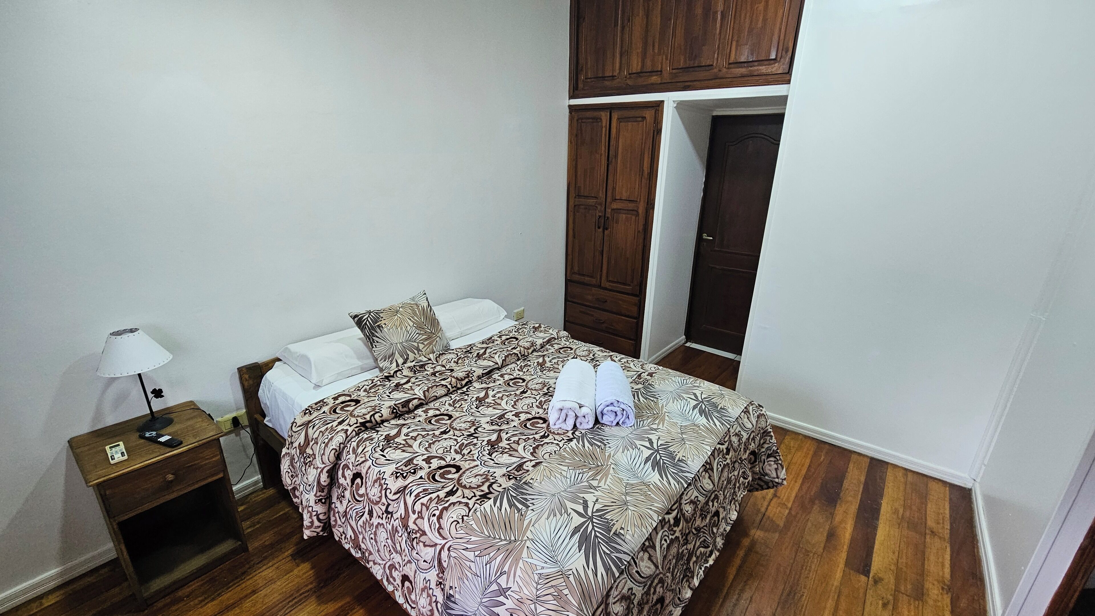 Une chambre à coucher avec un lit, une armoire en bois, une table de chevet et une lampe.