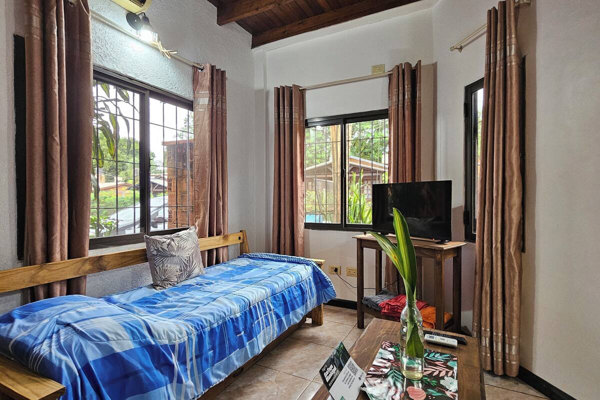 Ein Zimmer mit einem Bett, einem Fernseher, einem Tisch mit einer Vase und Vorhängen.