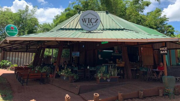 A rustic outdoor bar with a green roof, wooden tables, and potted plants. - Wicz Apart (Puerto Iguazú)