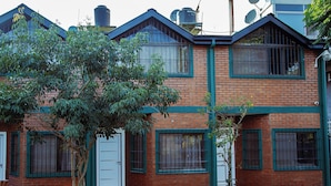A two-story brick building with a white door and windows with green frames. - Wicz Apart (Puerto Iguazú)