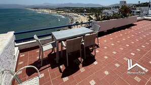 Une terrasse avec une table et des chaises donnant sur une plage et l’océan.