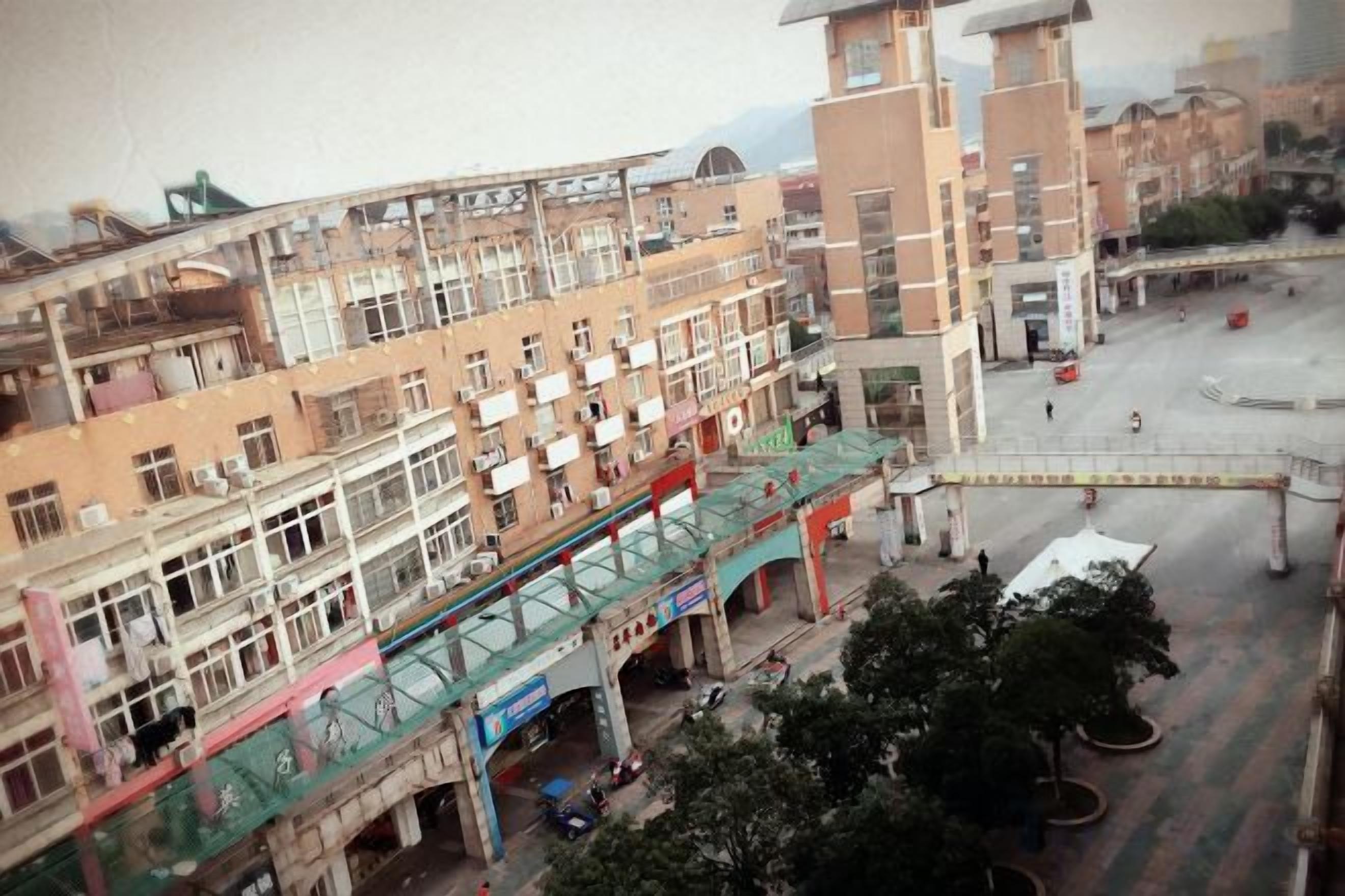 A multi-story building with a pedestrian bridge, a parking area, and a tower structure.
