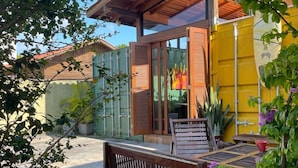 A wooden bench in a garden area with a yellow wall and a wooden pergola overhead. - Moçamba LODGE Contêiner (Florianópolis)