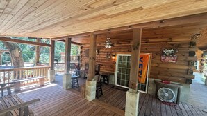 Un terrazzo in legno con zona salotto coperta, un cartello che riporta “Grizzly Lodge Welcome It's all good in the woods” e una ventola a destra.