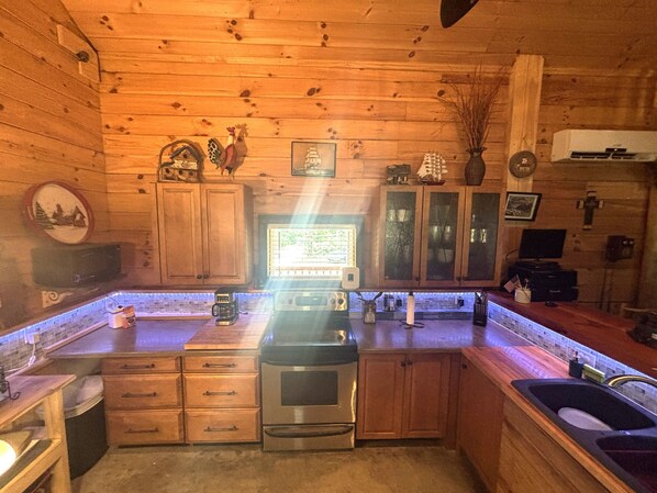 A wooden cabin kitchen with a stove, sink, cabinets, and a television.