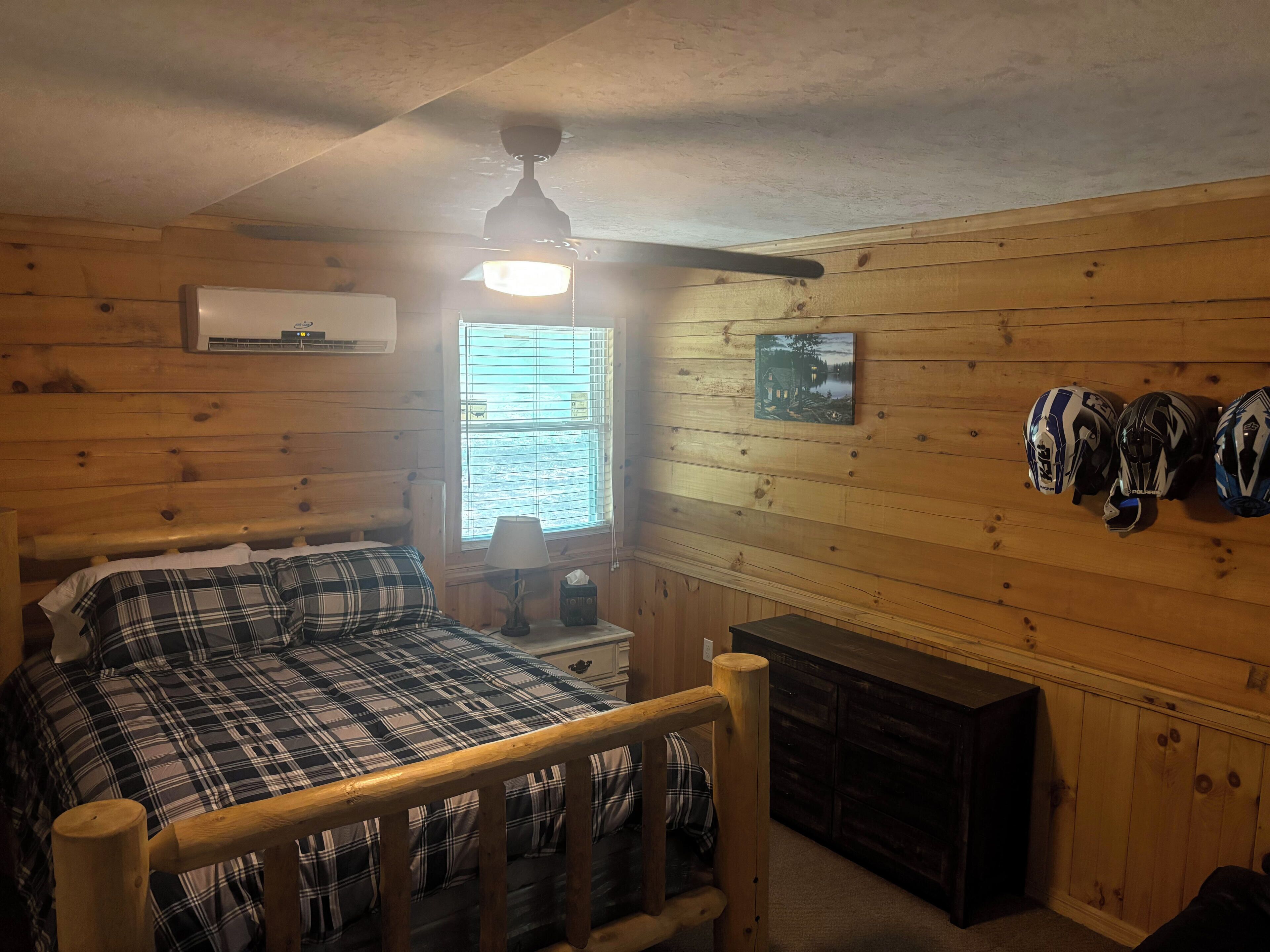 A cozy room with a bed, a window with blinds, a ceiling fan, and a wall-mounted air conditioner.