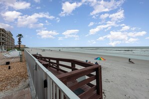 A beach with a wooden walkway, lounge chairs, and umbrellas. - Breathtaking Direct Oceanfront Views! Huge Community Pool, Private Beach Access! (New Smyrna Beach)