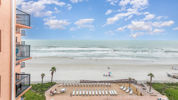 A beachfront hotel with a view of the ocean, a sandy beach, and a pool area with lounge chairs. - Breathtaking Direct Oceanfront Views! Huge Community Pool, Private Beach Access! (New Smyrna Beach)