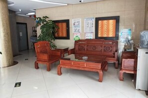 Un hall d’entrée avec un ensemble de meubles en bois comprenant un canapé, une table basse, une plante et des affiches informatives accrochées au mur.