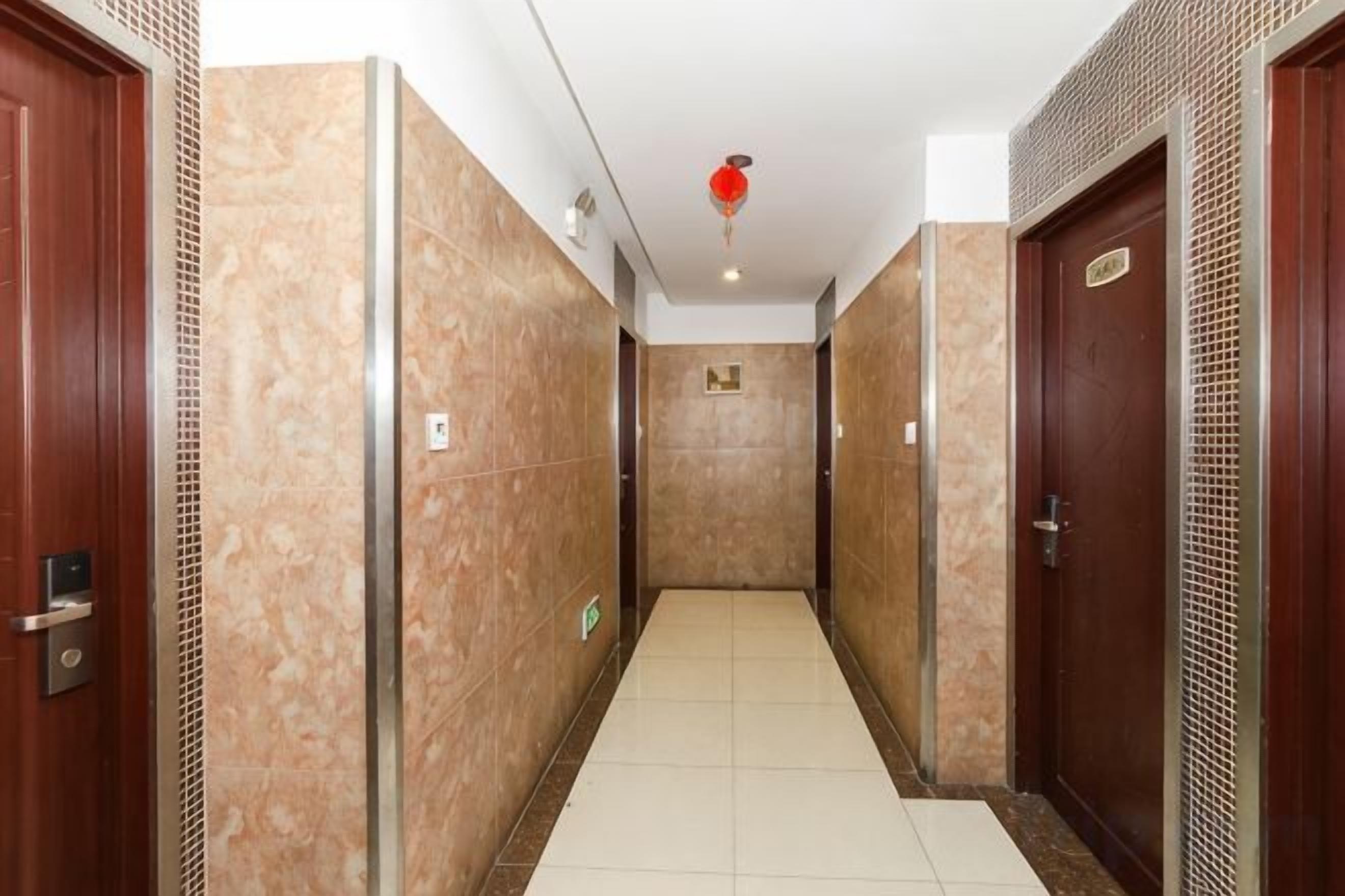 Un couloir avec des portes de chaque côté, un sol carrelé et un luminaire au plafond.