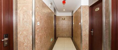 Un couloir avec des portes de chaque côté, un sol carrelé et un luminaire au plafond.