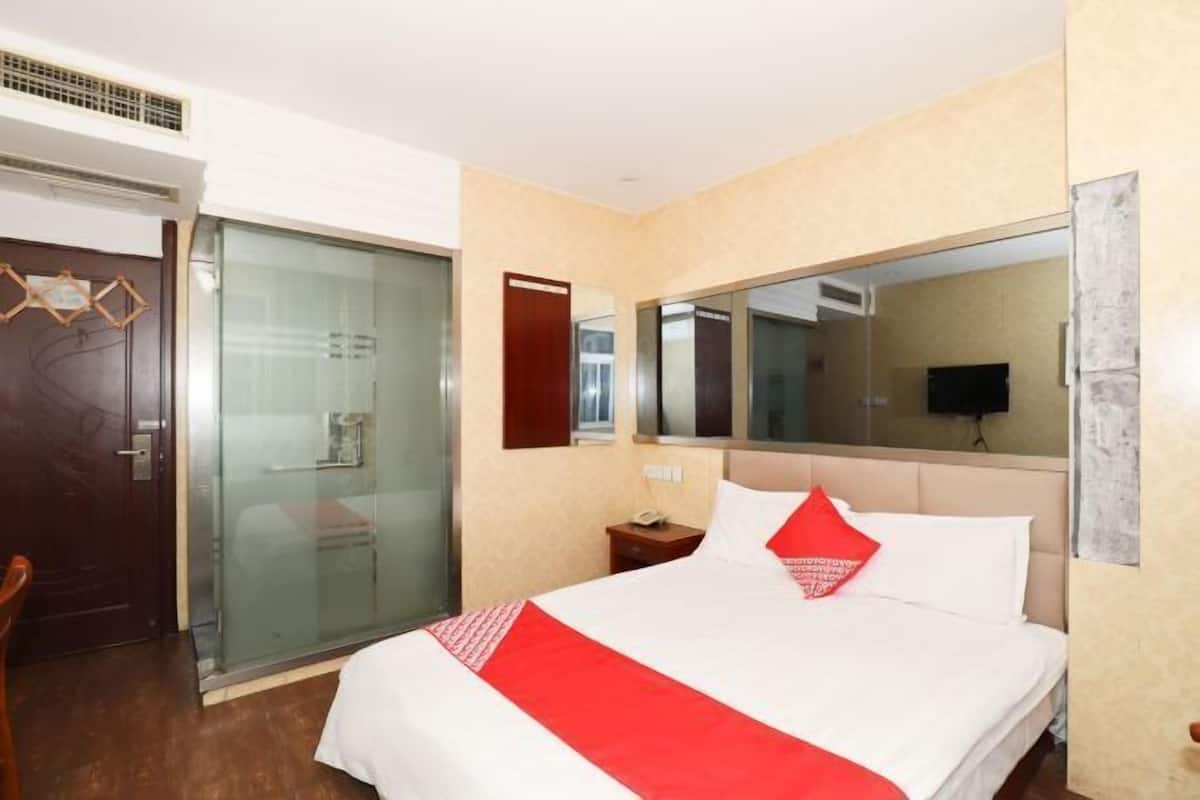 A hotel room with a bed, a mirror, a TV, and a sliding door.