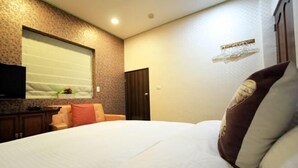 Una habitación de hotel con una cama grande, un televisor en la pared, un pequeño rincón de descanso y una ventana con persianas.