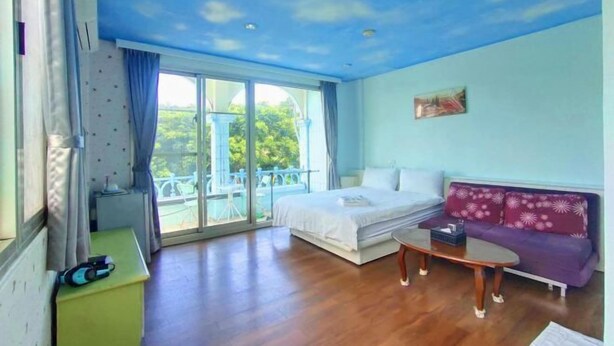 Una habitación con cama, sofá, una mesita y balcón con vistas a zonas verdes.