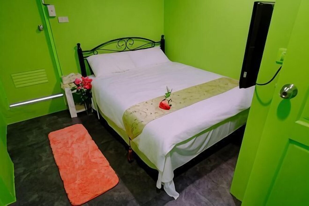 A room with a bed, a nightstand with a lamp, and a small orange rug.