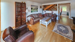 Ein Wohnzimmer mit einem braunen Ledersofa, einem weißen Couchtisch, einem gemusterten Teppich und einer Vitrine mit Dekoration.