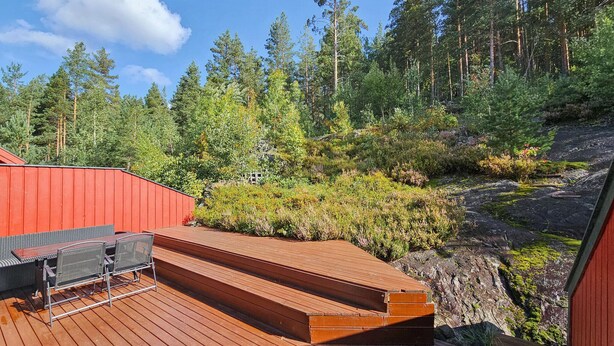 Eine Holzterrasse mit einem roten Gebäude im Hintergrund, umgeben von dichtem Wald und felsigem Gelände.